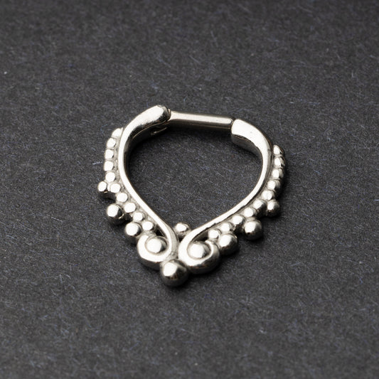 Close-up of a silver septum clicker with a teardrop shape and beaded embellishments, displayed on a dark background with a secure hinged clasp.