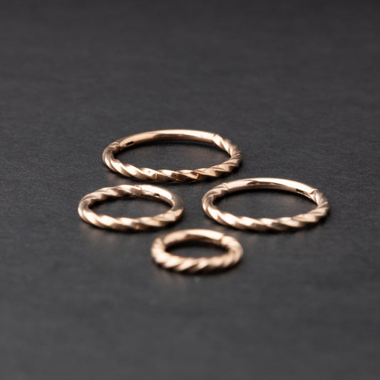 Close-up of a gold hinged ring with a twisted rope design, displayed on a dark background