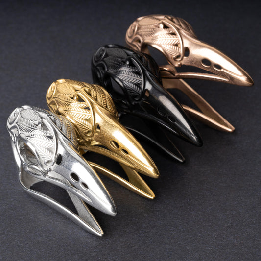 Raven skull ear hangers in silver, gold, black, and rose gold finishes, showcasing intricate feather engravings and polished details, displayed on a dark background.