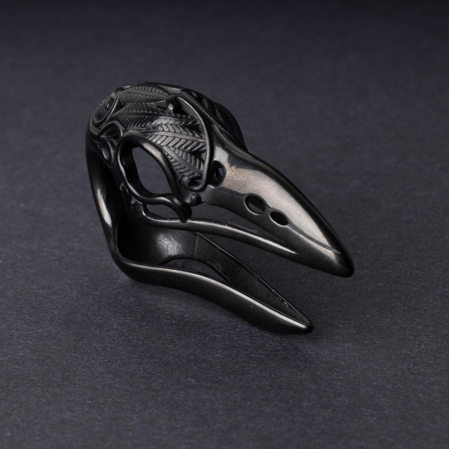 A black raven skull ear hanger showcasing intricate feather engravings and polished details, displayed on a dark background.