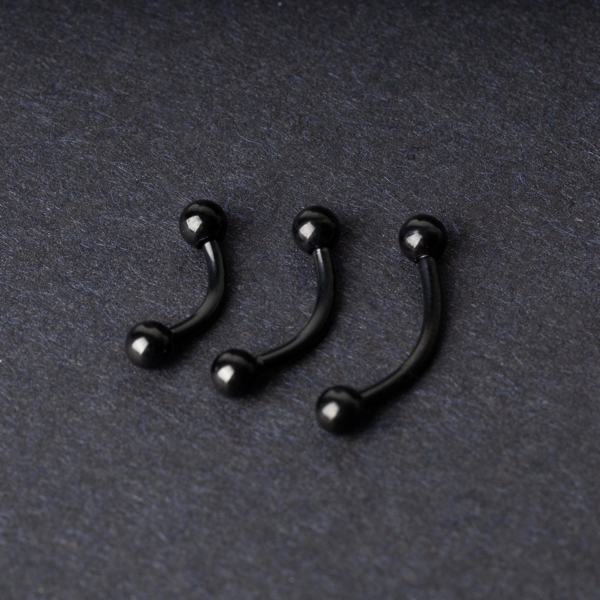 Three black curved barbells with threaded balls on each end, displayed on a dark background with a polished finish.