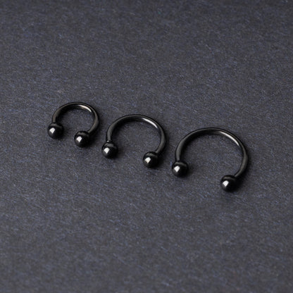 Three black stainless steel horseshoe hoops in varying sizes with threaded ball ends, displayed on a dark background.