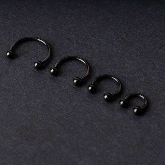 Four G23 titanium black horseshoe rings with ball ends in varying sizes, displayed on a dark background showcasing their polished finish.