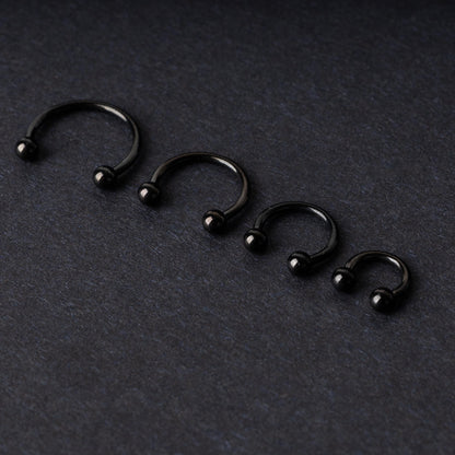 four G23 titanium black horseshoe rings with ball ends in varying sizes, displayed on a dark background showcasing their polished finish.