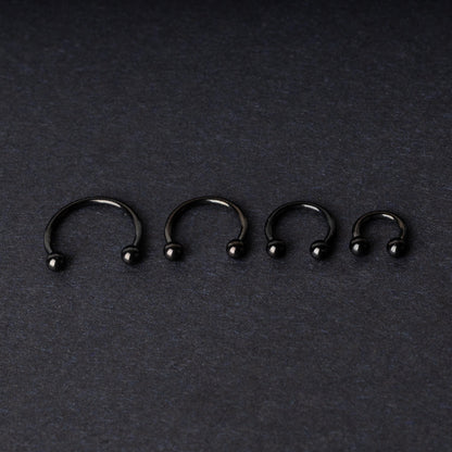 four G23 titanium black horseshoe rings with ball ends in varying sizes, displayed on a dark background showcasing their polished finish.