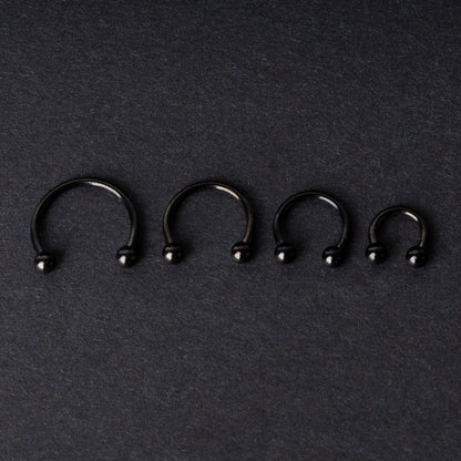 four G23 titanium black horseshoe rings with ball ends in varying sizes, displayed on a dark background showcasing their polished finish.