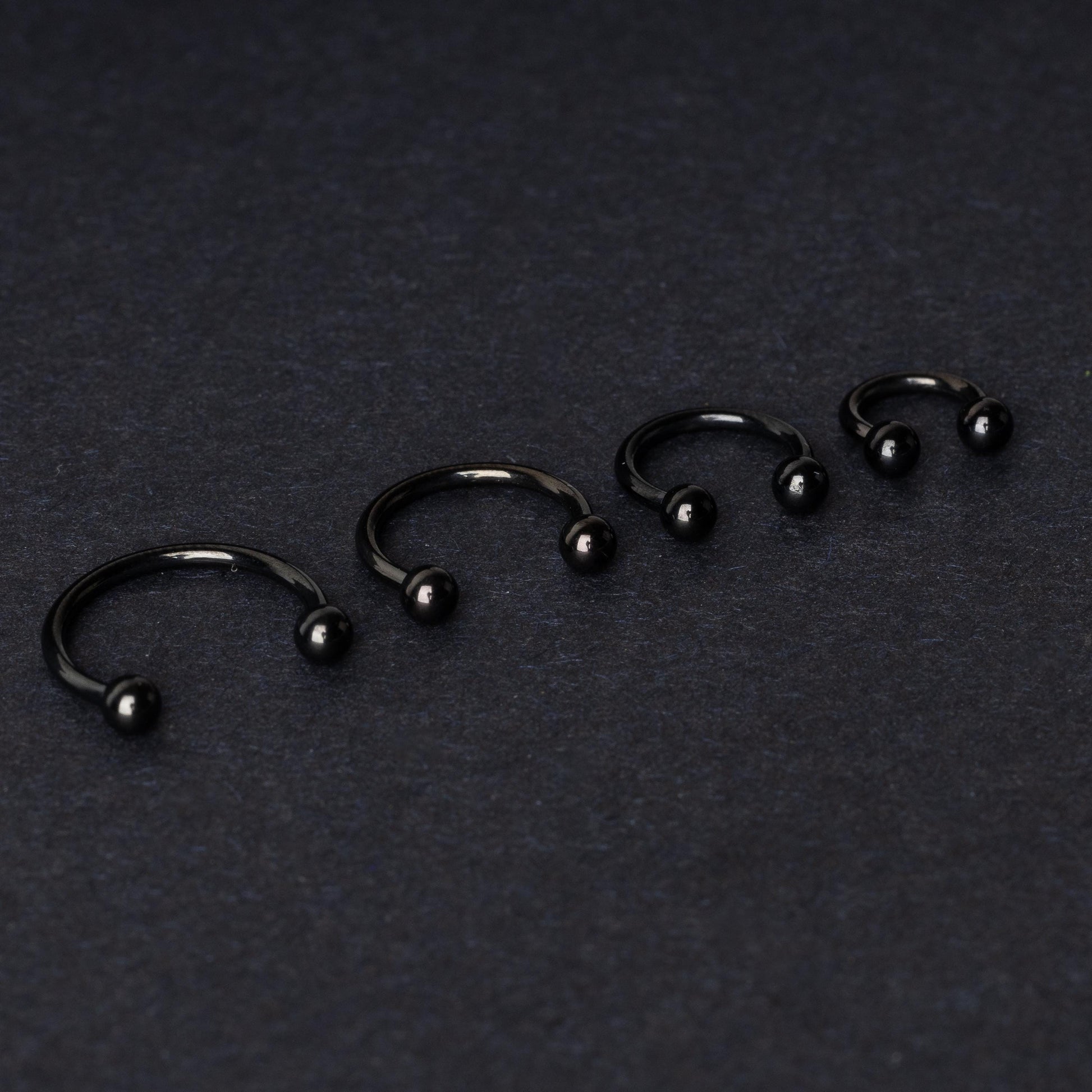 four G23 titanium black horseshoe rings with ball ends in varying sizes, displayed on a dark background showcasing their polished finish.