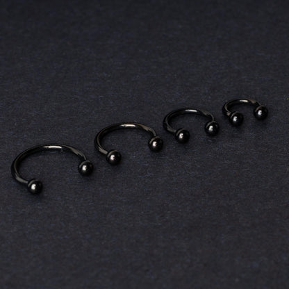 four G23 titanium black horseshoe rings with ball ends in varying sizes, displayed on a dark background showcasing their polished finish.