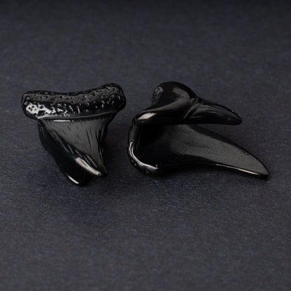 Close-up of black tooth ear weights featuring textured detailing, displayed on a dark background.

