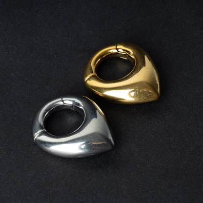 Two teardrop-shaped ear weights, one in polished silver and the other in polished gold, with a seamless hinge closure, displayed on a dark background.

