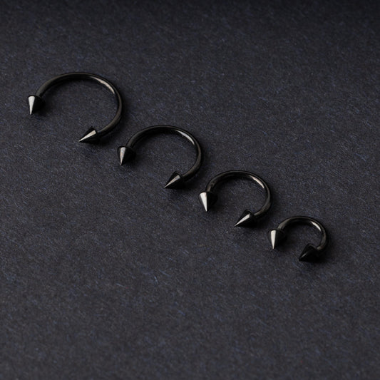 Four G23 titanium black horseshoe rings with spiked ends in varying sizes, displayed on a dark background showcasing their polished finish.