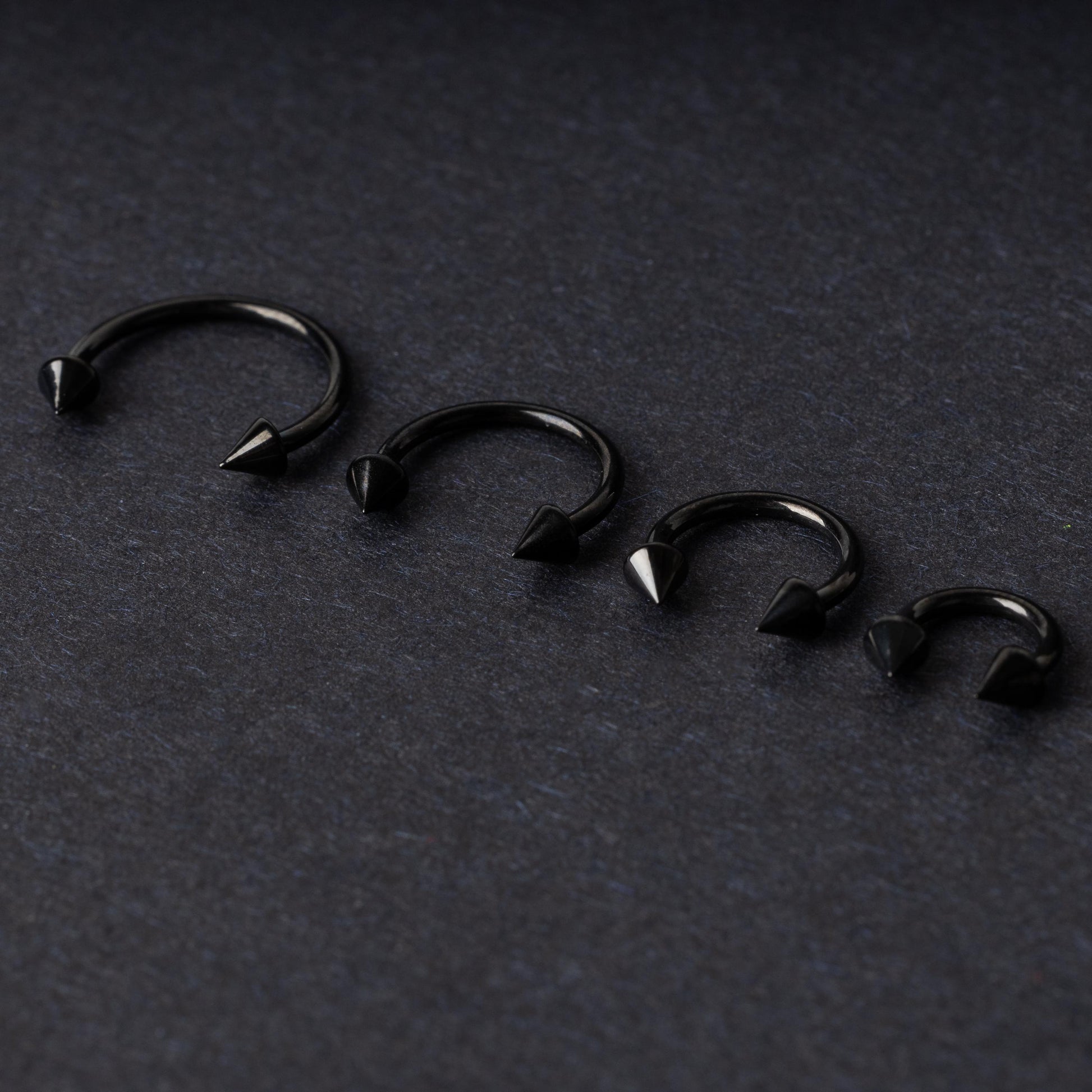 Four G23 titanium black horseshoe rings with spiked ends in varying sizes, displayed on a dark background showcasing their polished finish.