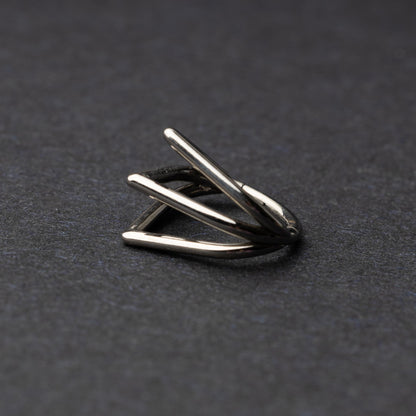 Close-up of a geometric septum clicker in silver, featuring a unique layered triangular design, displayed on a dark background.
