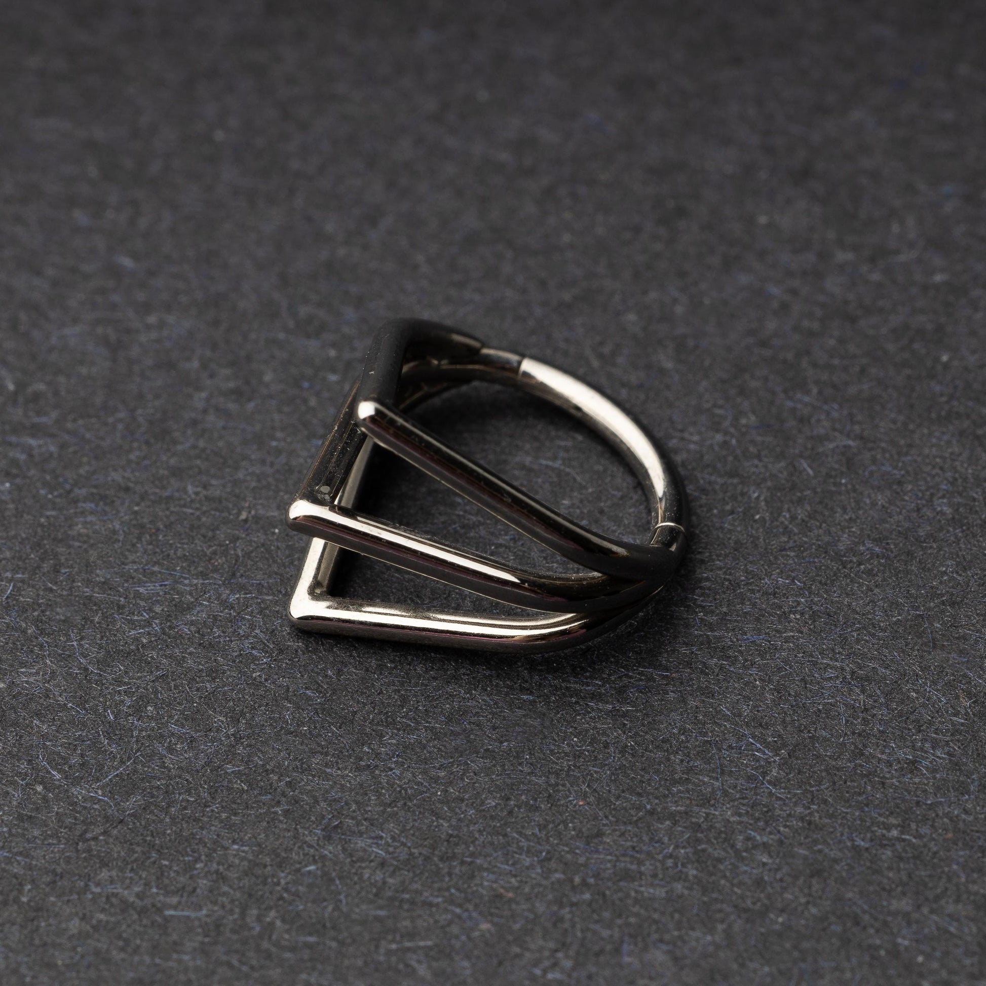 Close-up of a geometric septum clicker in silver, featuring a unique layered triangular design, displayed on a dark background.
