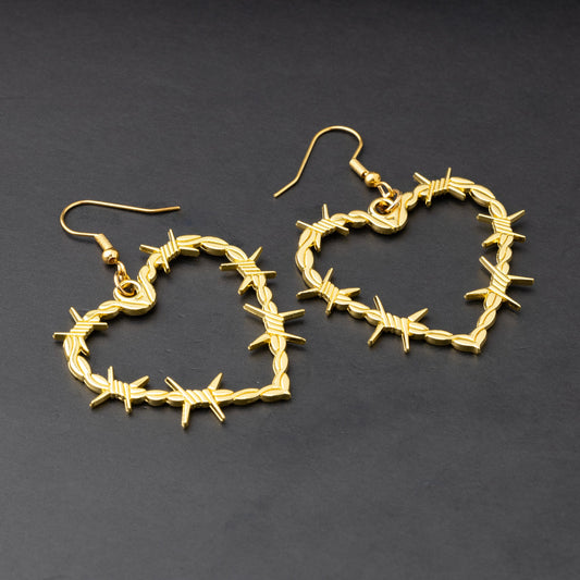 A pair of heart-shaped gold-tone hoop earrings designed with barbed wire detailing, displayed on a dark background.