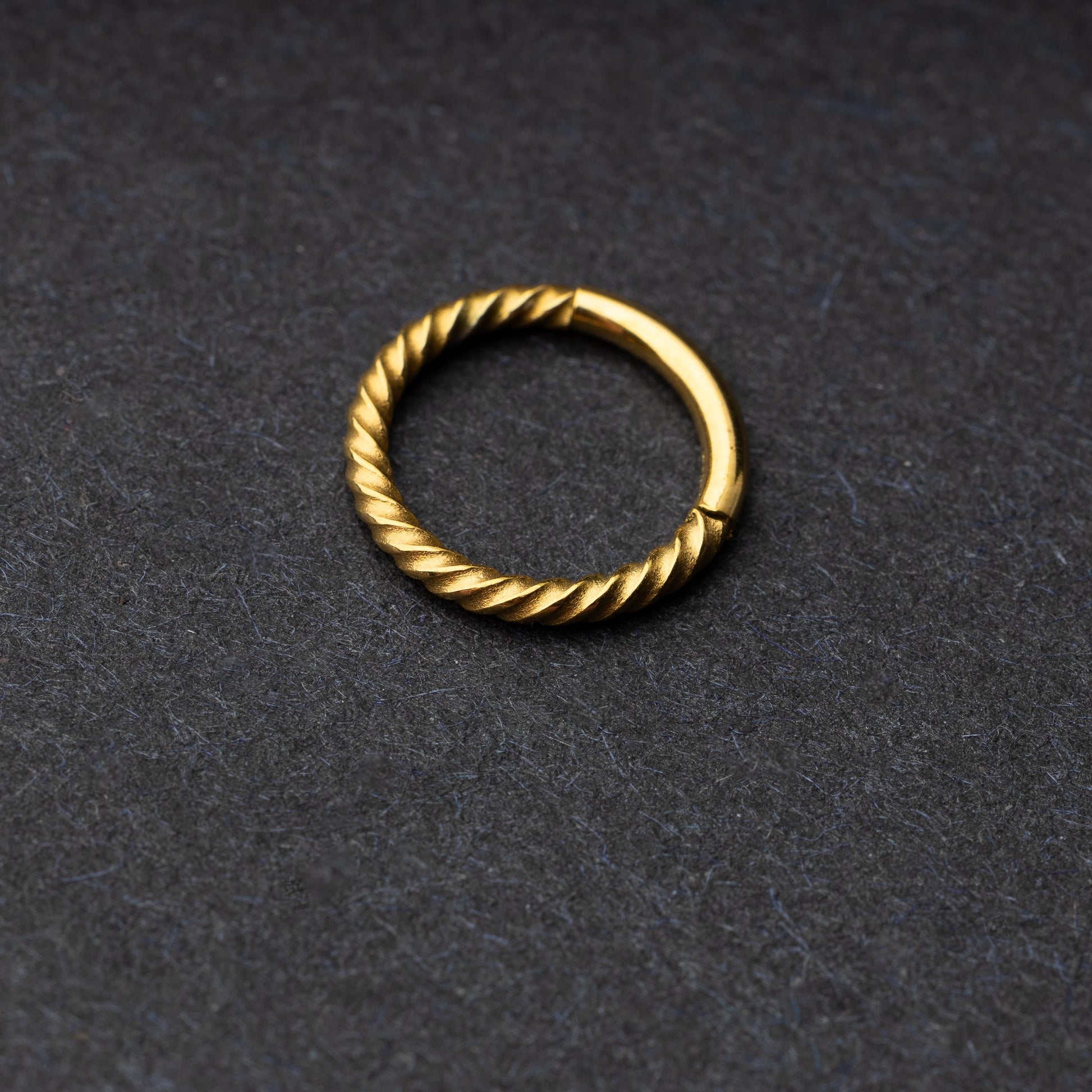 Twisted seamless hoop rings in gold finishes displayed on a dark background, highlighting their elegant and textured design.