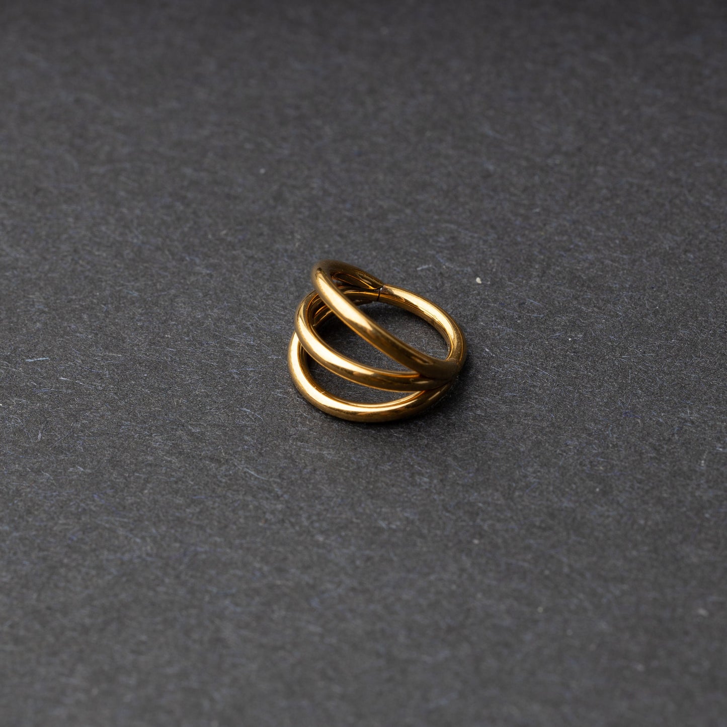 Four triple-band hoop septum clicker ring in gold finish, displayed on a dark background.
