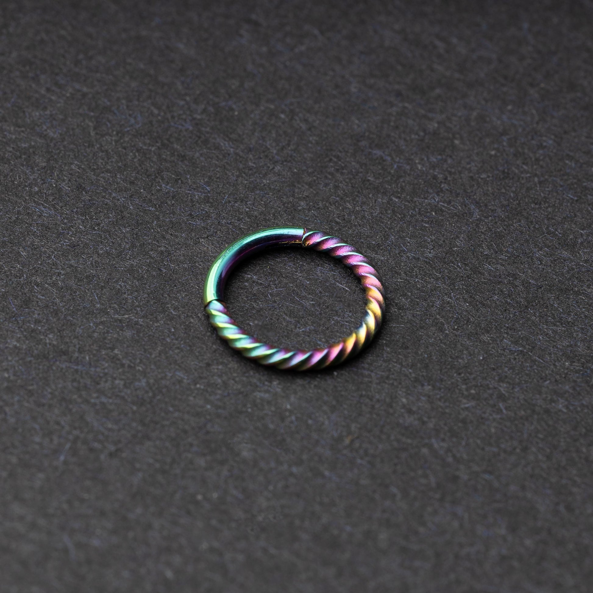 Twisted seamless hoop rings in rainbow finishes displayed on a dark background, highlighting their elegant and textured design.