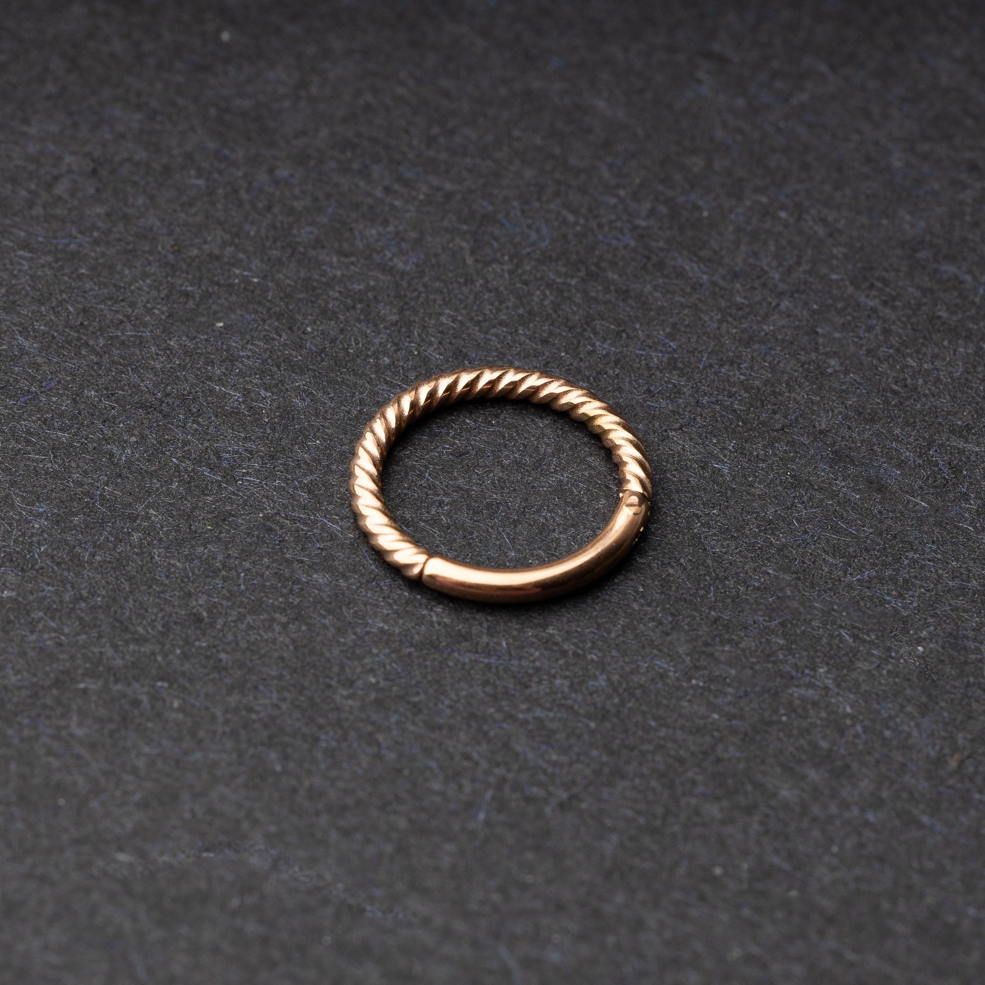 Twisted seamless hoop rings in rose gold finishes displayed on a dark background, highlighting their elegant and textured design.