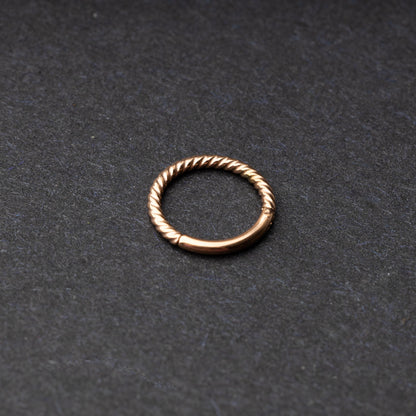 Twisted seamless hoop rings in rose gold finishes displayed on a dark background, highlighting their elegant and textured design.