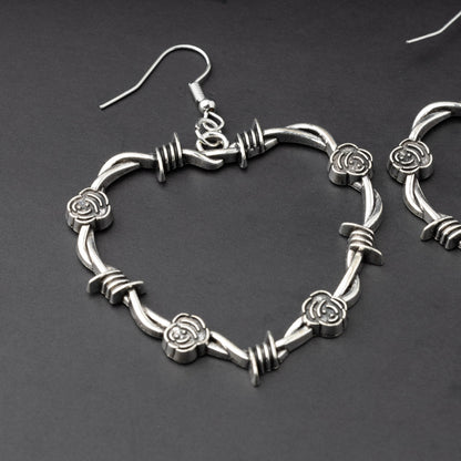 A single heart-shaped silver hoop earring designed with barbed wire detailing, displayed on a dark background.