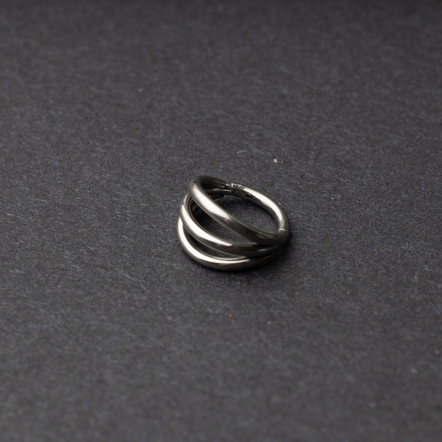 Four triple-band hoop septum clicker ring in silver finish, displayed on a dark background.
