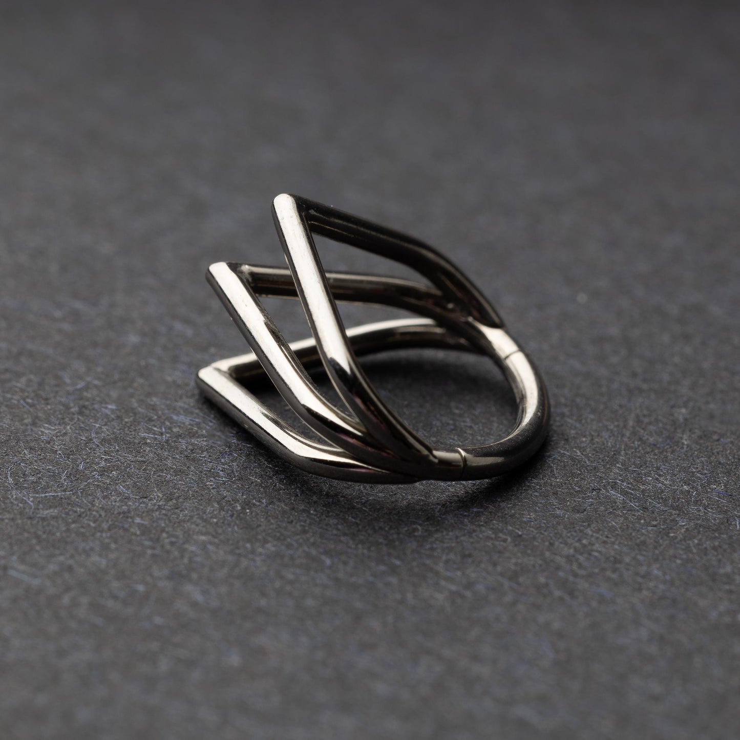 Close-up of a geometric septum clicker in silver, featuring a unique layered triangular design, displayed on a dark background.
