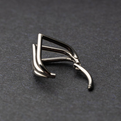 Close-up of a geometric septum clicker in silver, featuring a unique layered triangular design, displayed on a dark background.
