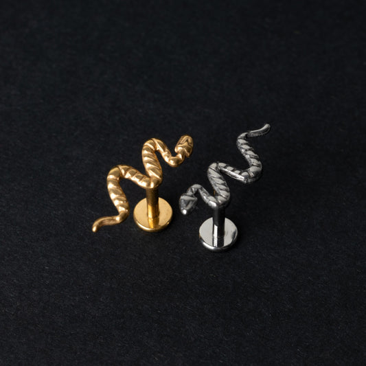 Gold-tone and silver-tone snake labret bars with intricate coiled snake designs displayed on a dark background.

