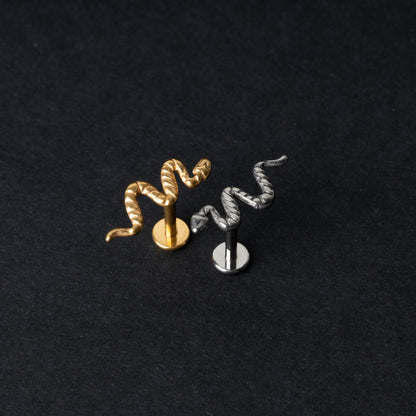 Gold-tone and silver-tone snake labret bars with intricate coiled snake designs displayed on a dark background.

