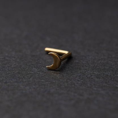 A gold-tone crescent moon nose stud with a curved design for secure and comfortable wear, displayed on a dark background.