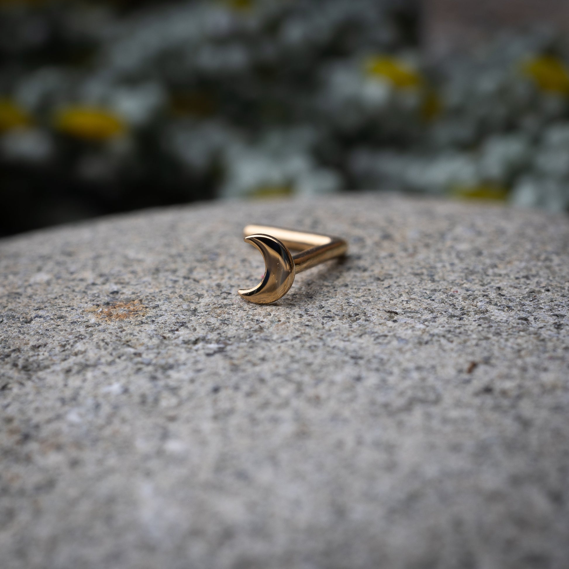 A gold-tone crescent moon nose stud with a curved design for secure and comfortable wear, displayed on a stone background.