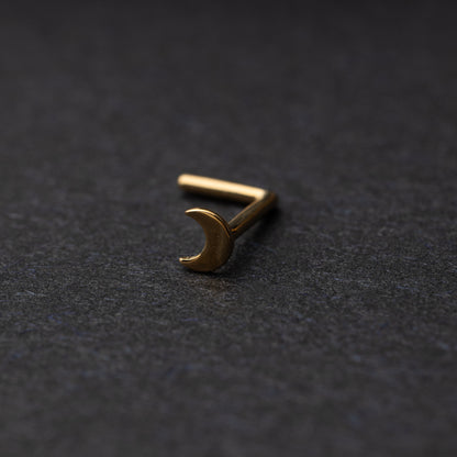 A gold-tone crescent moon nose stud with a curved design for secure and comfortable wear, displayed on a dark background.