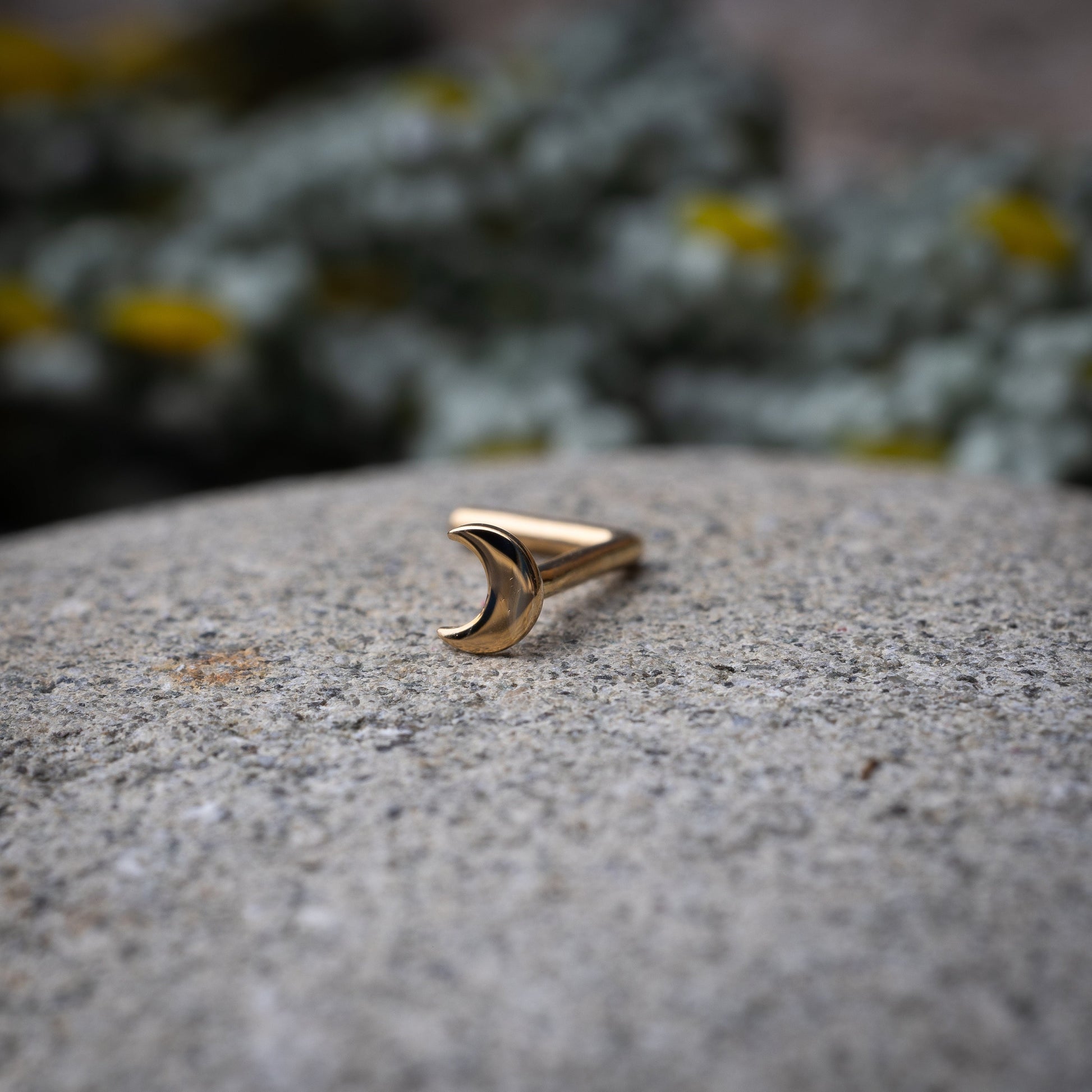 A gold-tone crescent moon nose stud with a curved design for secure and comfortable wear, displayed on a stone background.