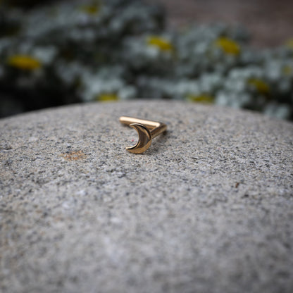 A gold-tone crescent moon nose stud with a curved design for secure and comfortable wear, displayed on a stone background.