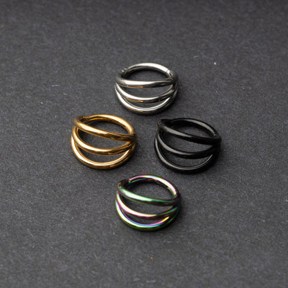 Four triple-band hoop septum clicker rings in gold, silver, black, and rainbow finishes displayed on a dark background.
