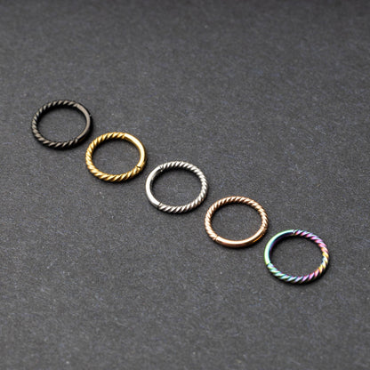 Twisted seamless hoop rings in black, gold, silver, rose gold, and rainbow finishes displayed on a dark background, highlighting their elegant and textured design.