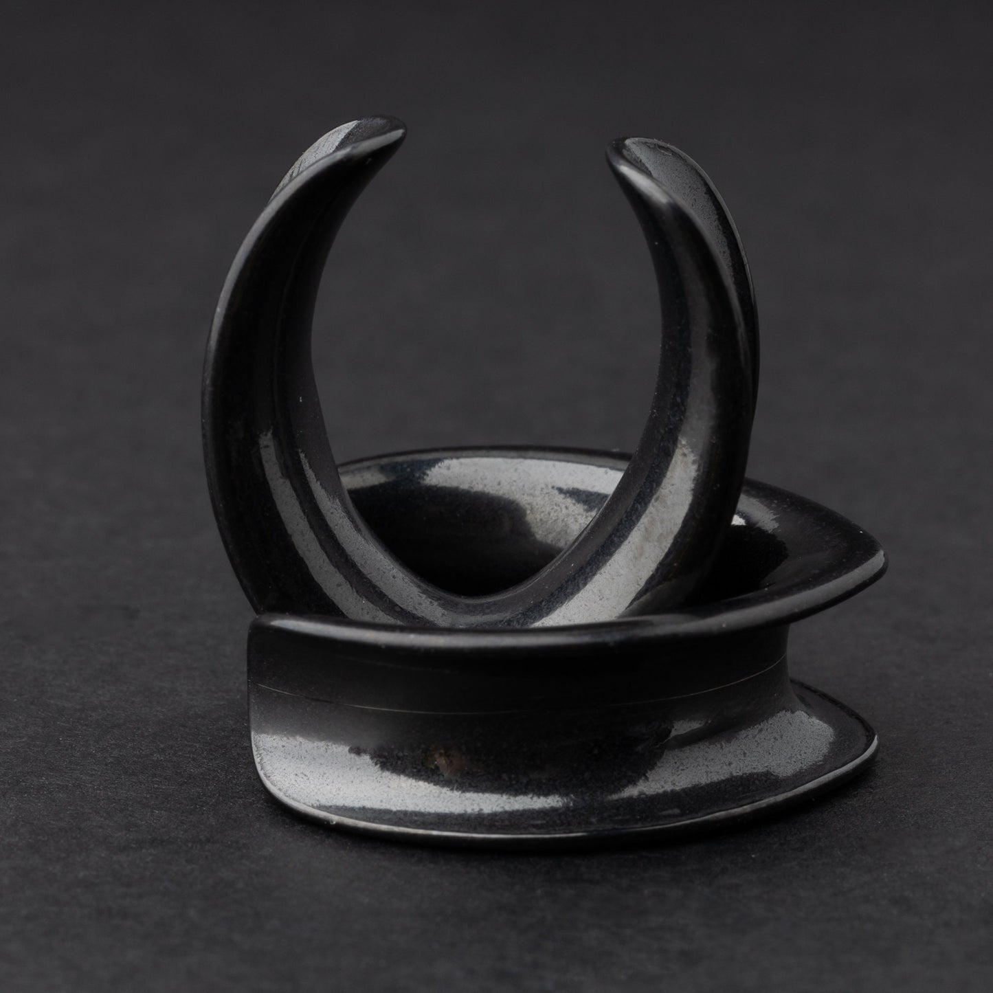 A collection of double-flared metal tunnels for stretched ears in black finish, displayed on a dark background.
