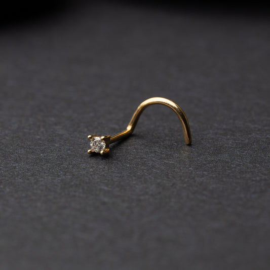 A gold-tone nose stud with a clear prong-set gem, featuring a curved design for secure wear, displayed on a dark background.