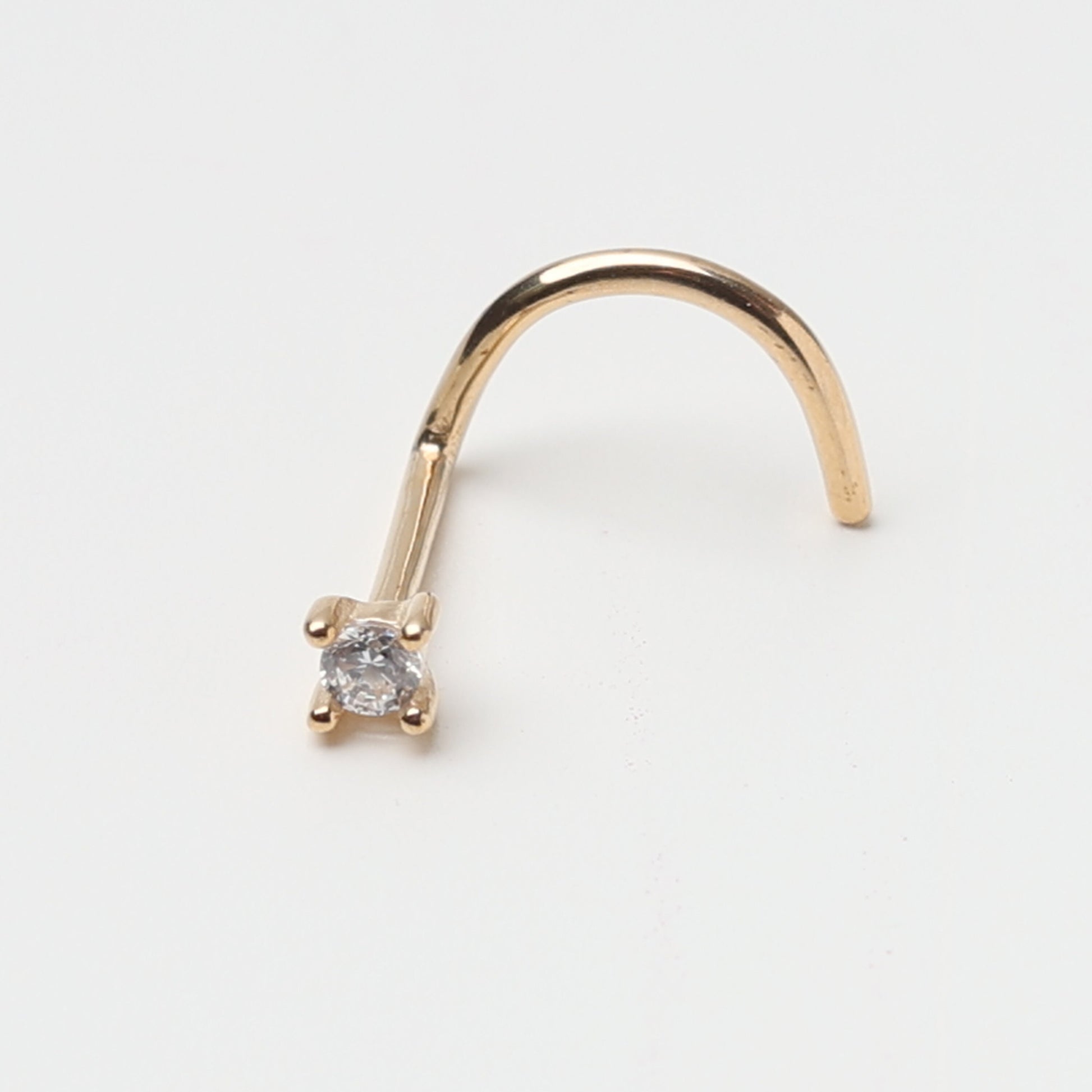 A gold-tone nose stud with a clear prong-set gem, featuring a curved design for secure wear, displayed on a white background.