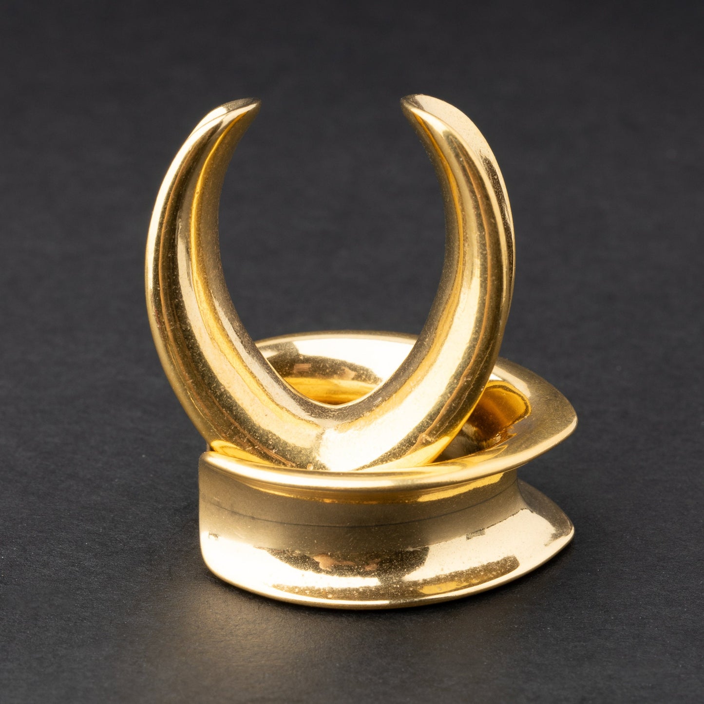 A collection of double-flared metal tunnels for stretched ears in gold finish, displayed on a dark background.

