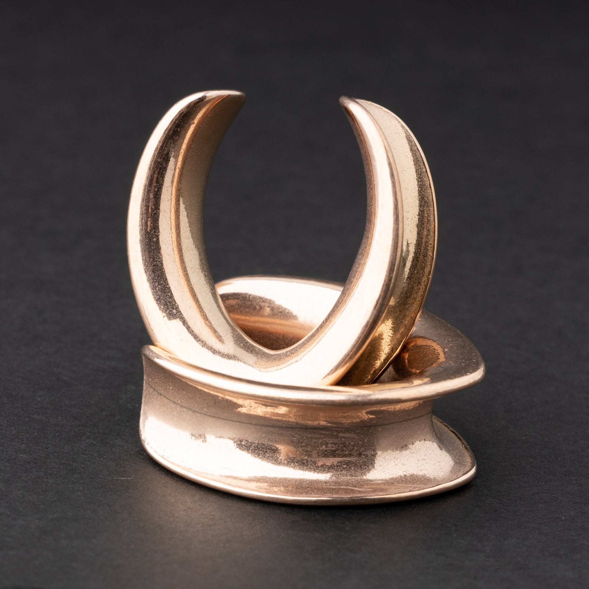 A collection of double-flared metal tunnels for stretched ears in rose gold finish, displayed on a dark background.
