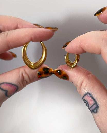 A collection of double-flared metal tunnels for stretched ears in gold, silver, black and rose gold  finish, displayed on a dark background.
