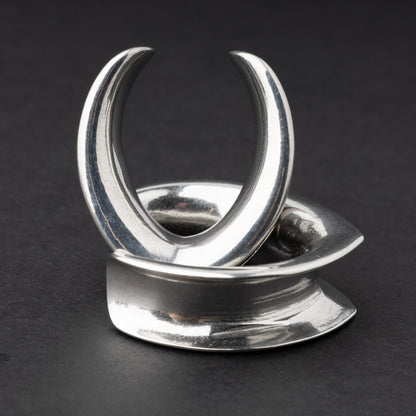 A collection of double-flared metal tunnels for stretched ears in silver finish, displayed on a dark background.
